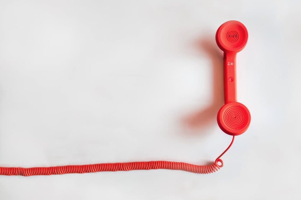 Ein roter Telefonhörer hängt an einer hellen Wand