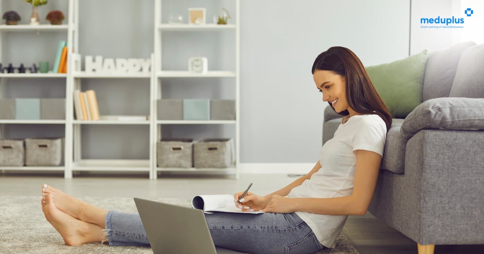 Frau sitzt zu Hause vor dem Sofa und lernt mit Laptop und Notizblock